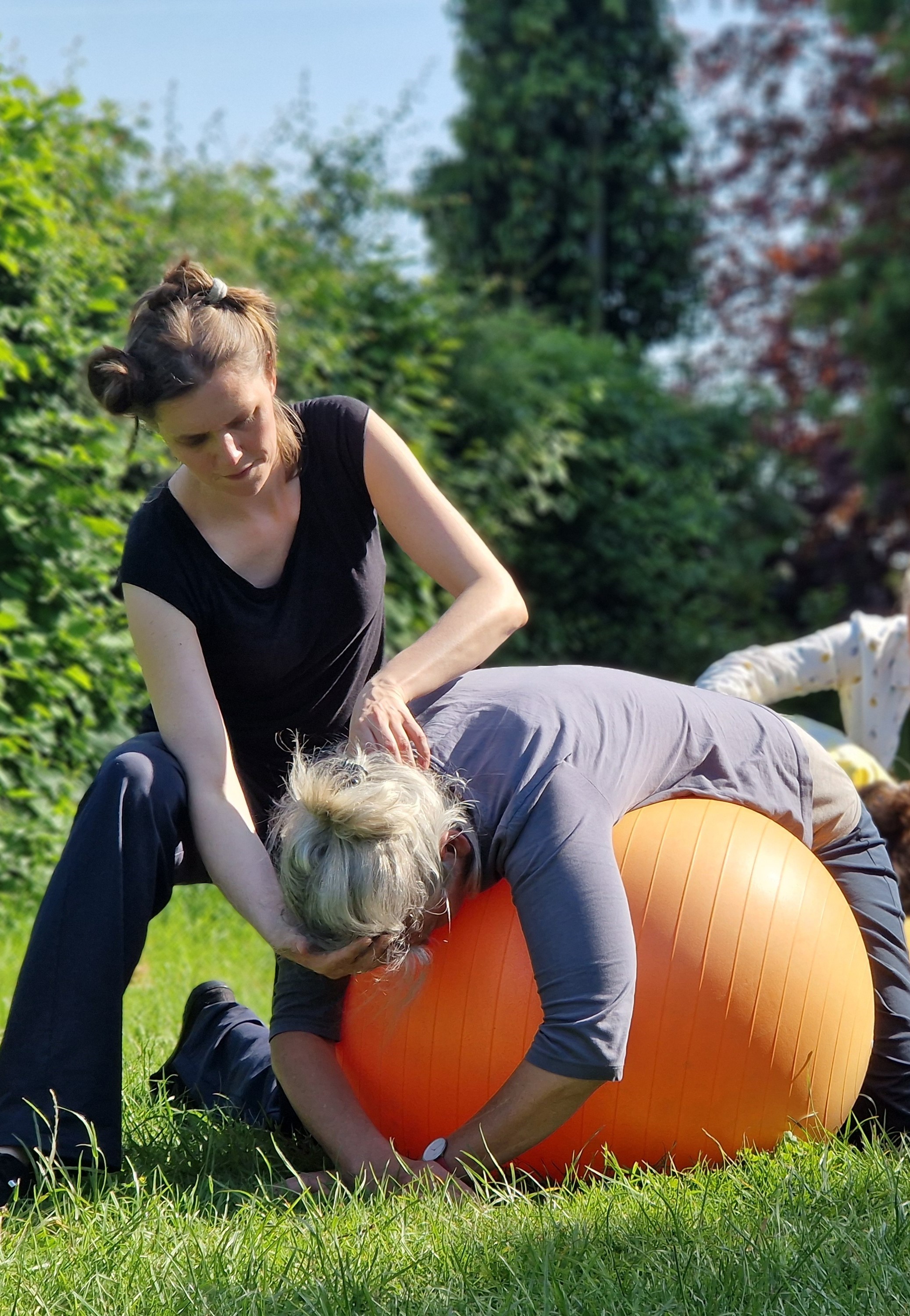 Alexandertechnik im Freien: Lehrerin begleitet Teilnehmerin mit achtsamer Handführung am Gymnastikball